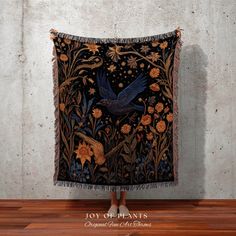 a tapestry hanging on the wall with a bird and flowers design in gold, blue, orange and black