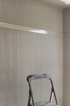 a metal step stool sitting in front of a wall with vertical blinds on it's sides