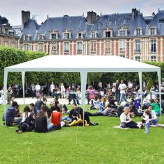 a group of people sitting on top of a lush green field under a white tent