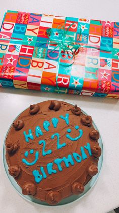 a chocolate birthday cake sitting on top of a table next to a wrapped gift box