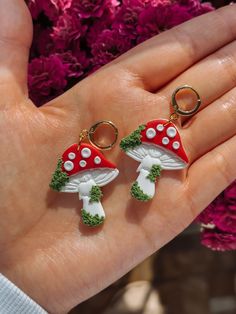 a hand holding two red and white mushrooms on it's fingers, with pink flowers in the background