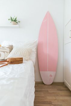 a pink surfboard sitting on top of a bed next to a white wall and wooden floor