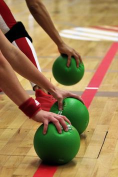 two people holding green balls on top of a basketball court with red and white lines