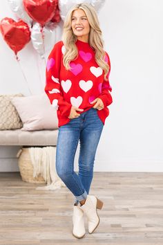 a woman standing in front of balloons wearing a red sweater with hearts printed on it