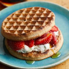 a waffle sandwich with strawberries and cream on a blue plate next to a glass of syrup