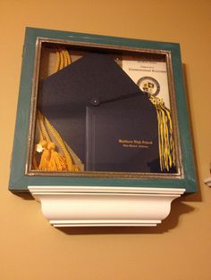 a graduation cap and tassel in a frame on the wall above a mantle with an ornament