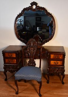 an antique vanity and chair with a mirror on the wall above it, in front of a wooden floor