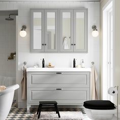 a white bathroom with black and white checkered flooring, two sinks, an armoire cabinet, and a bathtub