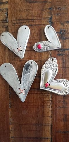 four silver heart shaped brooches sitting on top of a wooden table