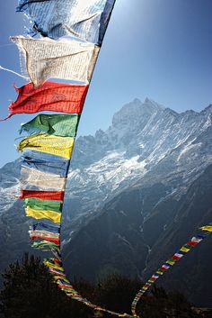 there are many colorful flags hanging from the side of a mountain with snow capped mountains in the background