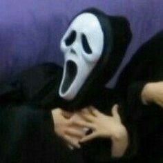 a person wearing a ghost mask with their hands in the air while sitting on a couch