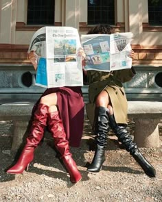 two women sitting on a bench reading the paper while wearing knee high boots and over - the - knee boots