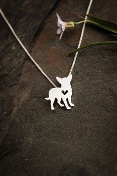 a necklace with a dog on it sitting on top of a rock next to a flower