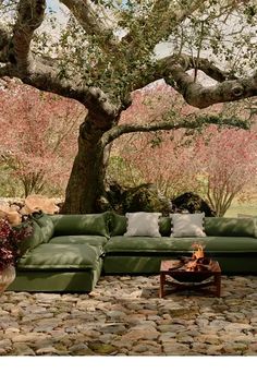 a large green couch sitting under a tree next to a fire pit on top of a stone floor