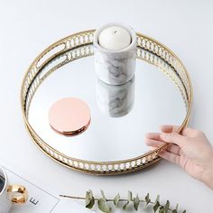 a person's hand holding a candle in front of a round glass tray on a table