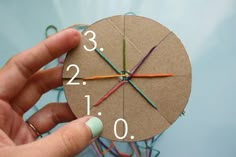 a hand is holding a clock made out of paper and yarn with numbers on it