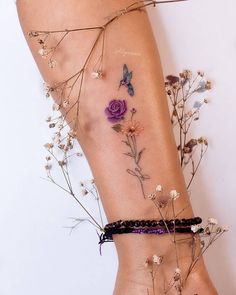 a woman's tattoo with flowers and butterflies on her leg, next to dried plants