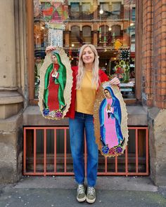 a woman holding up two crocheted virgin marys in front of a store