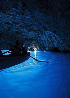 two people are in a boat at the entrance to a cave that is lit up with blue light