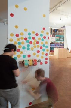 two men are working on some artwork in an art gallery, one is painting the wall