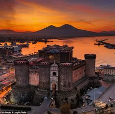 an aerial view of a castle with mountains in the background and water around it at sunset