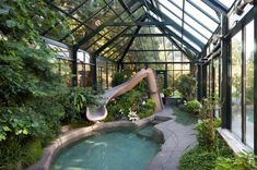 the inside of a greenhouse with a hot tub and glass walls on one side, surrounded by greenery