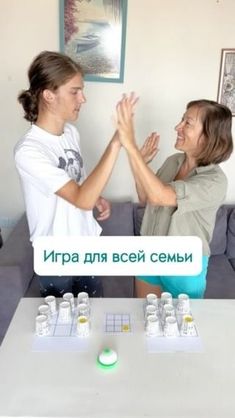 two people standing in front of a table with cups on it and one person holding their hands up