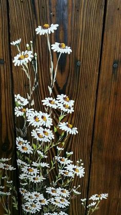 a painting of daisies in a vase on a wooden table next to a fence