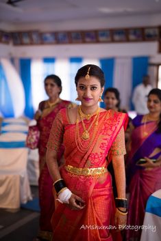 a woman in a red and gold sari standing next to other women wearing white gloves