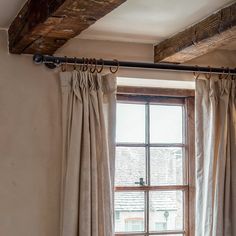 an open window with curtains hanging in front of it and a wooden beam on the ceiling