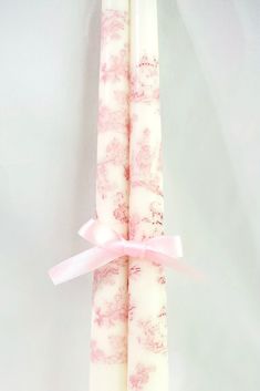 two candles with pink and white designs on them, tied together by a pink ribbon