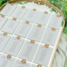 a gold and white wedding seating chart on a table with greenery in the background