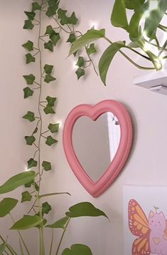 a heart shaped mirror hanging on the wall next to a potted plant with green leaves