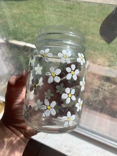 a person holding up a glass jar with flowers painted on the inside and outside of it