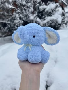 a small blue stuffed elephant sitting on top of someone's hand in the snow