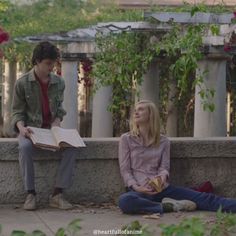 two people sitting on the ground with one reading a book and another looking up at something