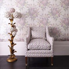 a chair next to a lamp in front of a wallpapered room with flowers on it