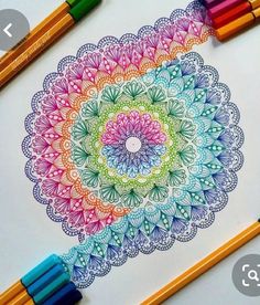 colored pencils and crayons on top of a paper with an intricate design