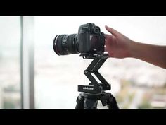 a hand holding a camera on top of a tripod in front of a window