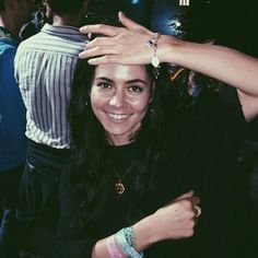 a woman is holding her hand up to her head and smiling at the camera with other people in the background