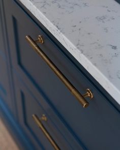 a marble counter top with brass handles in a blue cabinet door style kitchen island area