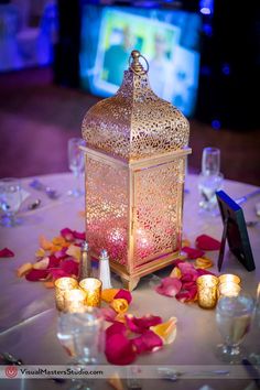 a lit candle is on top of a table with rose petals and wine glasses in front of it