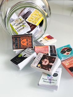 a glass jar filled with lots of books on top of a white table next to a stack of books