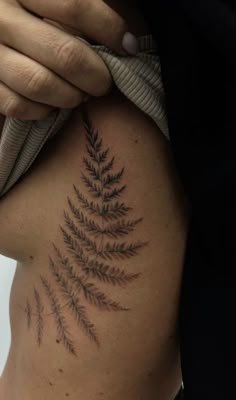 a woman's back with a fern tattoo on her left side ribcage