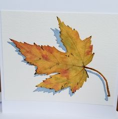 an orange and yellow leaf is on a white card with watercolor pencils in it