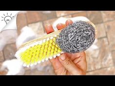 a hand holding a yellow and white brush in front of a brick wall with snow on it