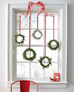 a red chair sitting in front of a window with wreaths hanging from the windowsill