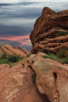 the sun is setting over some rocks in the desert with grass and bushes growing on them