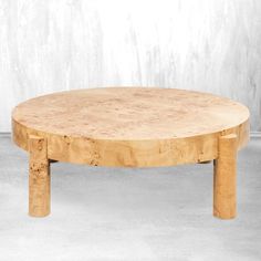 a round wooden table sitting on top of a cement floor next to a white wall