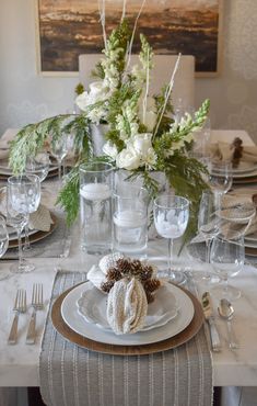 a table set for christmas dinner with white flowers and greenery in the centerpiece